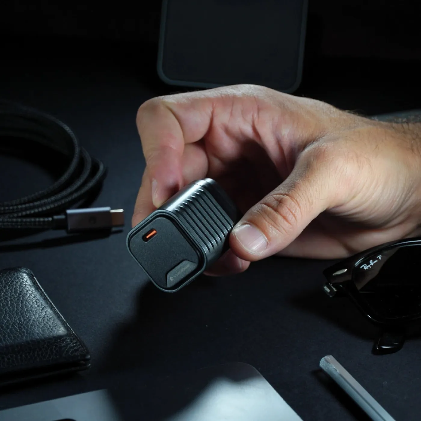 A hand holding the Supertiny over a desk with a wallet and cable.