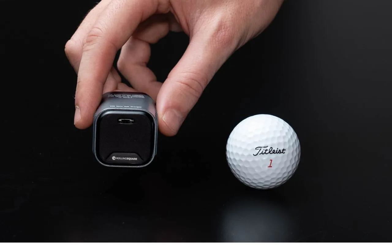 A hand holding the Supertiny next to a golf ball.